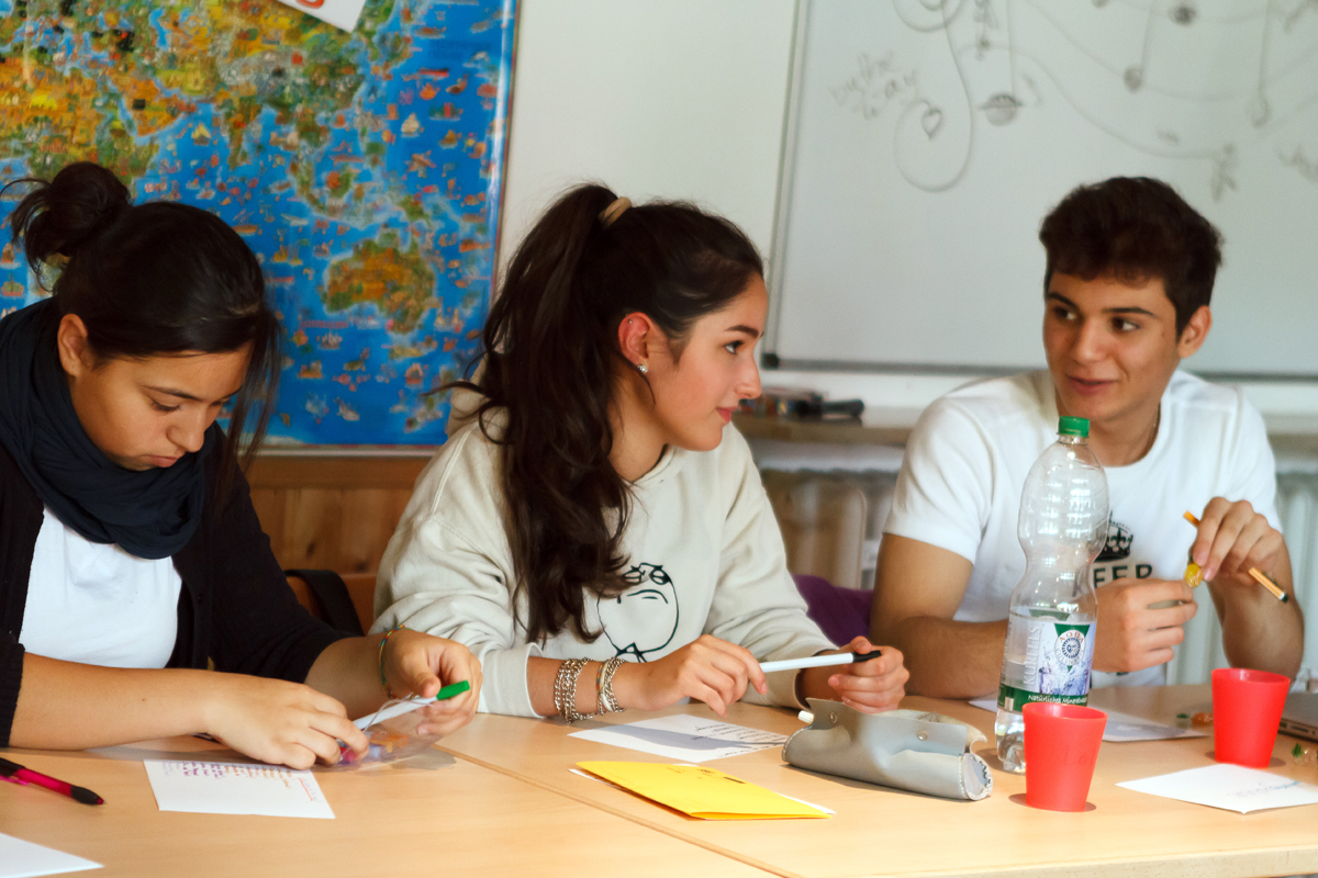 3 Schüler*innen diskutieren in einem Klassenzimmer